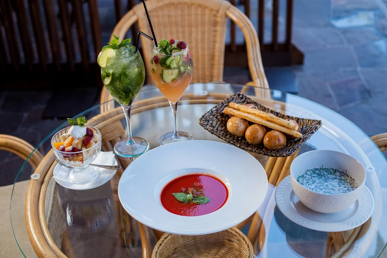 a plate of food sitting on top of a glass table, at the terrace, soup, ratatouille style, drinks