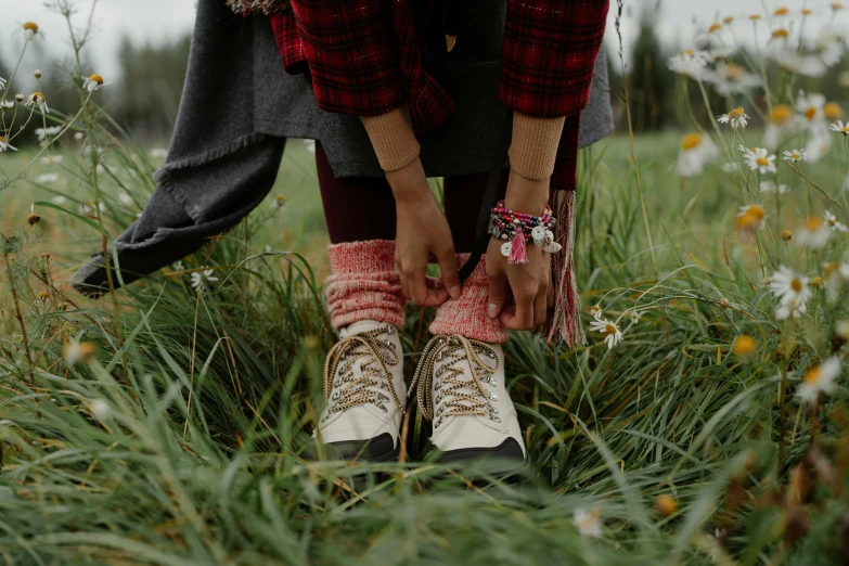 a woman sitting on top of a lush green field, a photo, by Emma Andijewska, trending on pexels, maroon doc marten boots, wrapped in cables and flowers, lumberjack flannel, walking on grass