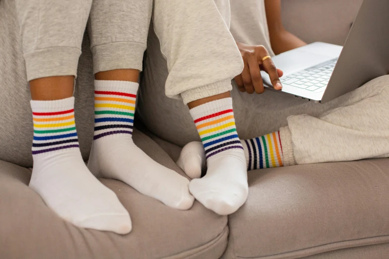 a couple of people that are sitting on a couch, inspired by Okuda Gensō, trending on pexels, computer art, striped socks, close-up shot from behind, pastel faded grey rainbow, working on her laptop