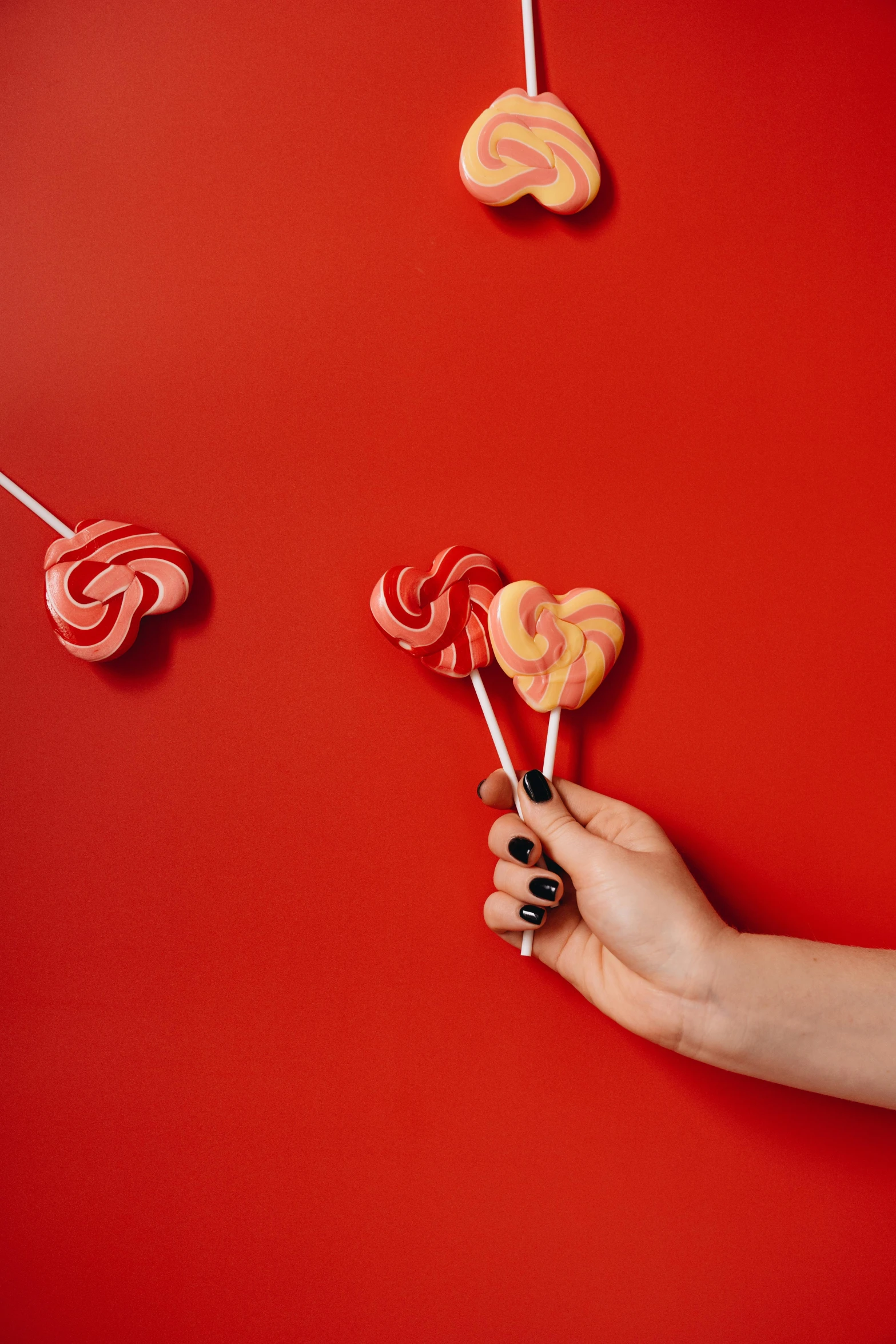 a person holding a bunch of heart shaped lollipops, inspired by Louise Bourgeois, trending on pexels, graffiti, red wall, 4k polymer clay food photography, swirly, 🐿🍸🍋