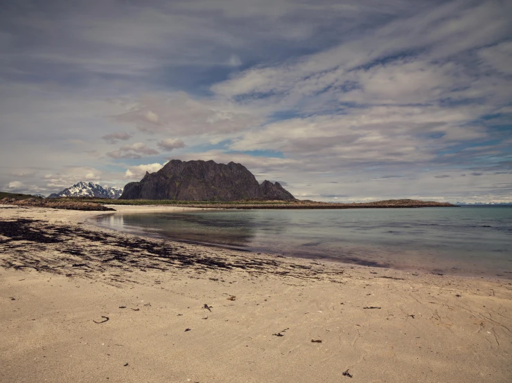 a sandy beach with a mountain in the background, by Roar Kjernstad, pexels contest winner, in a beachfront environment, grey, vintage glow, whealan
