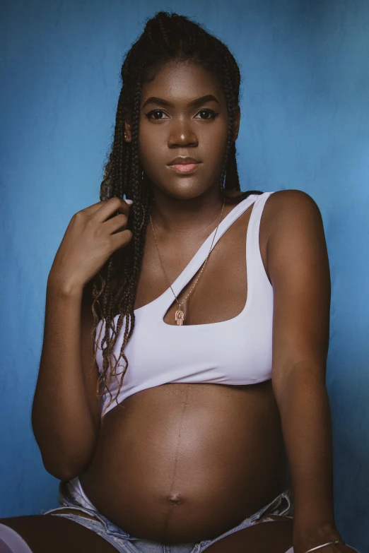 a pregnant woman sitting on top of a bed, an album cover, by Lily Delissa Joseph, unsplash, happening, wearing a crop top, ( brown skin ), transgender, white soft leather model