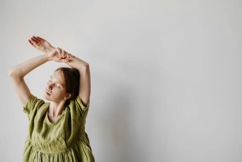 a woman in a green dress standing in front of a white wall, unsplash, light and space, couple dancing, nursing, raising an arm, woman with braided brown hair