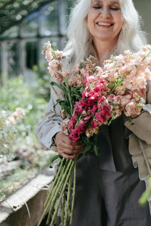 a woman holding a bunch of flowers in her hands, by Sara Saftleven, trending on unsplash, pink and grey muted colors, gardens, large tall, clothes made out of flower