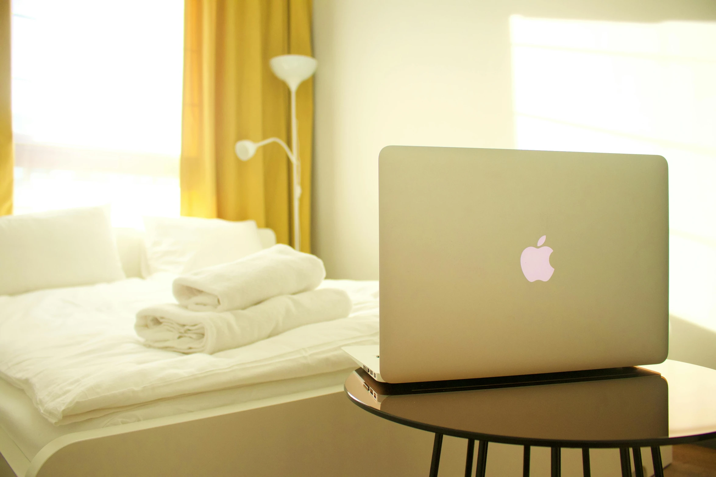 a laptop computer sitting on top of a wooden table, pexels, cream - colored room, golden apple, white bed, yellow