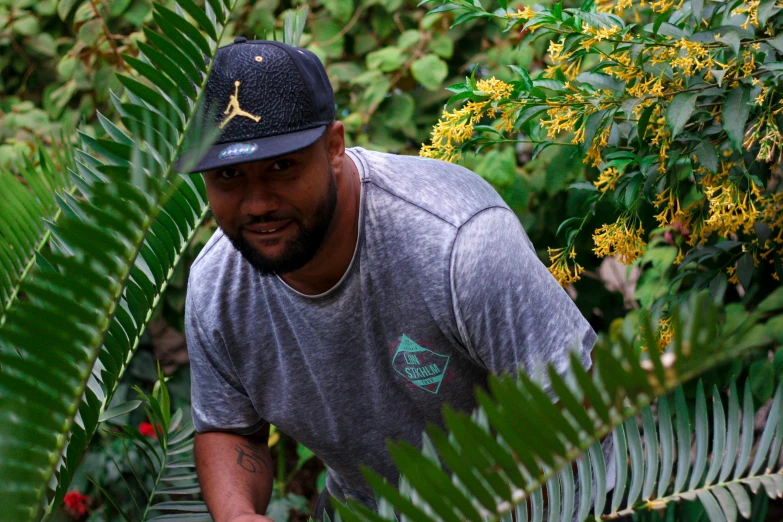 a man holding a tennis racquet on top of a lush green field, a portrait, hurufiyya, in marijuanas gardens, avatar image, fern, wearing a navy blue utility cap