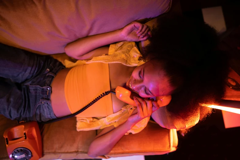 a woman laying on a couch talking on a phone, a portrait, inspired by Nan Goldin, pexels contest winner, process art, pink and orange neon lights, willow smith zendaya, yellow lighting, scene from live action movie