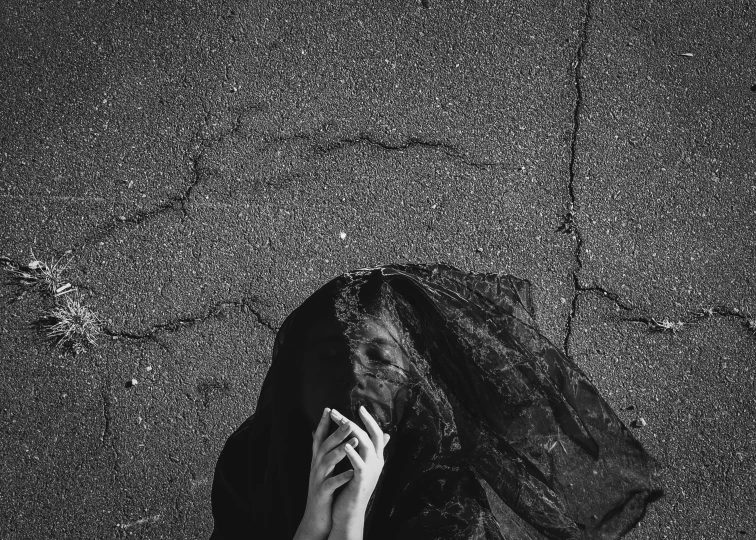 a black and white photo of a person covering their face, by Lucia Peka, pexels contest winner, conceptual art, on the concrete ground, praying with tobacco, black slime, funeral veil