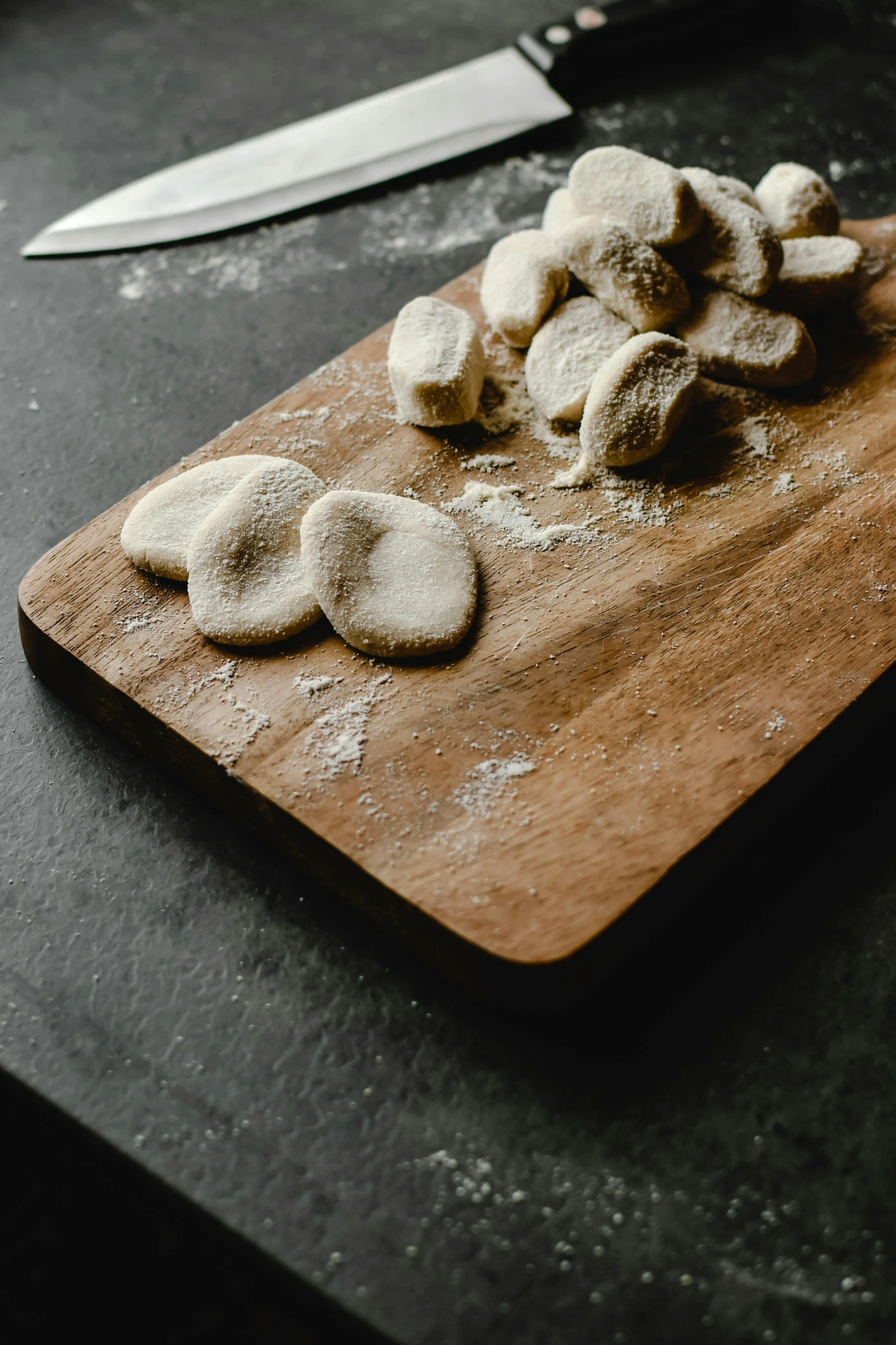 a wooden cutting board topped with cookies next to a knife, inspired by Enzo Cucchi, unsplash, process art, puffballs, white stones, stew, medium close up shot