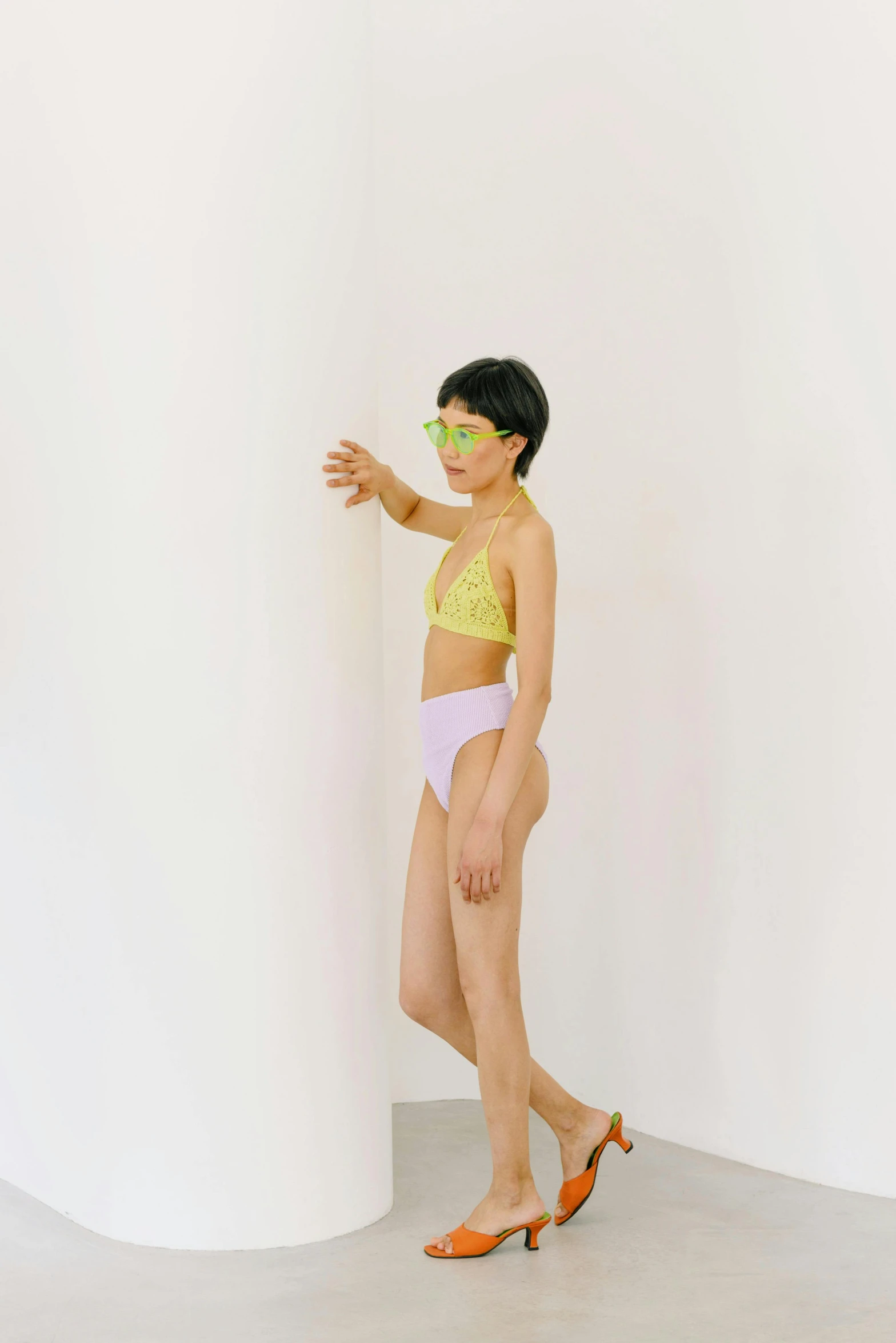 a woman standing in front of a white wall, inspired by Ren Hang, wearing pearl neon bikini, lime and violet, nonbinary model, pastel