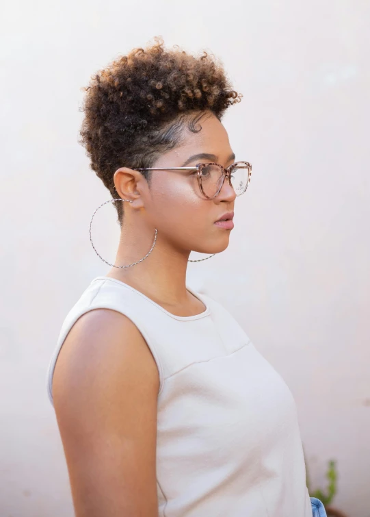 a woman with glasses standing in front of a white wall, by Lily Delissa Joseph, curly and short top hair, profile image, square rimmed glasses, mixed-race woman