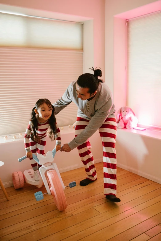 a woman teaching a little girl how to ride a bike, a picture, inspired by The Family Circus, pexels contest winner, wearing pajamas, asian man, brightly lit pink room, red and white stripes