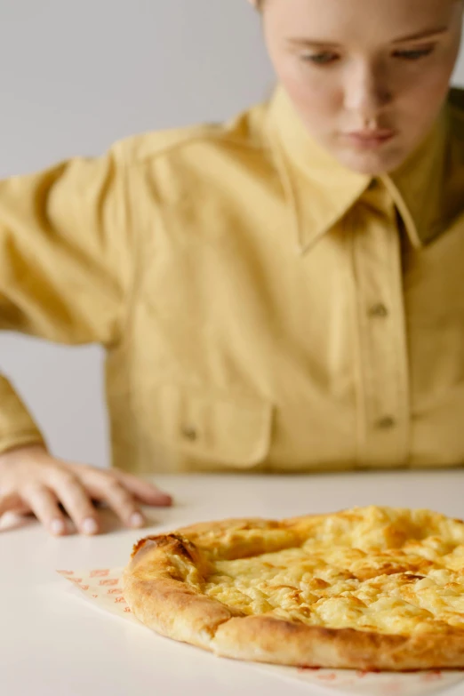 a young boy sitting at a table with a pizza in front of him, trending on unsplash, realism, yellow, vomit, close up to a skinny, ignant