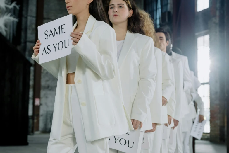 a group of people standing next to each other holding signs, inspired by Vanessa Beecroft, unsplash, aestheticism, labcoat, in white lettering, issey miyake, young women