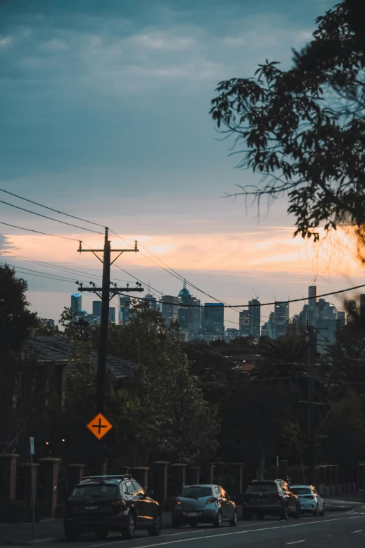 a street filled with lots of traffic next to tall buildings, by Lee Loughridge, unsplash contest winner, caulfield, powerlines, humid evening, skyline