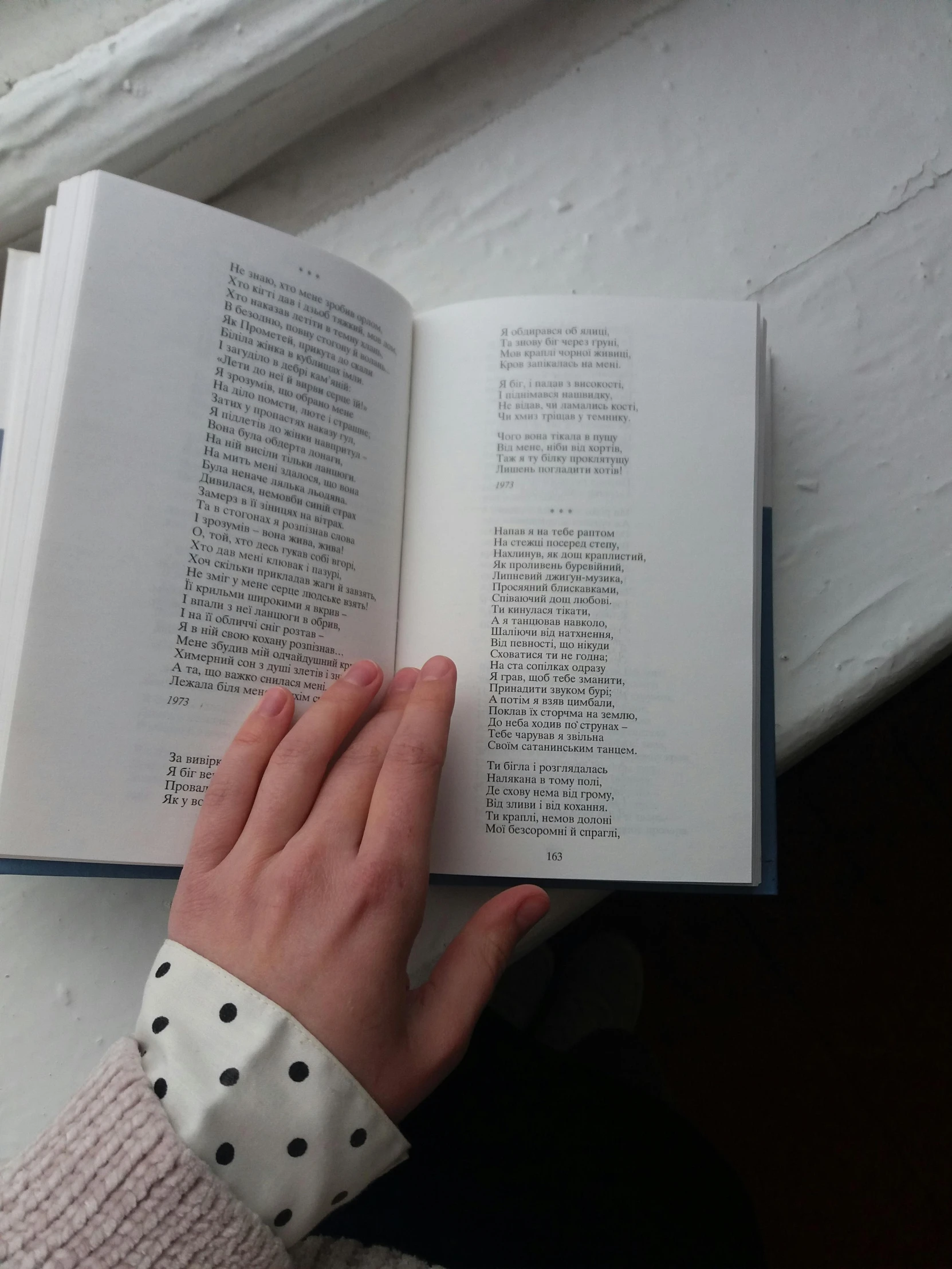 a person reading a book on a window sill, corrected hand, very very very pale skin, pointing, text