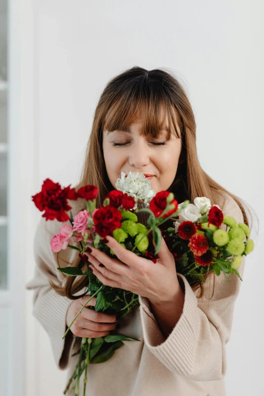 a woman holding a bunch of flowers in front of her face, smelling good, white and red color scheme, slightly smiling, on a white table