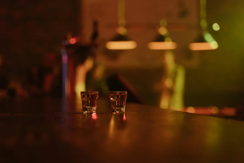 two shot glasses sitting on top of a wooden table, pexels, neon bar lights, todd hido, high quality photo, speakeasy