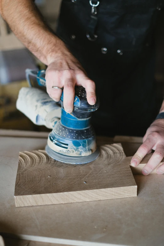a man sanding a piece of wood with a sander, a woodcut, trending on pexels, blue woodcut print, levitating sand, curvy build, oak
