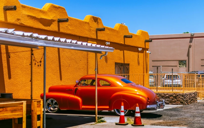 a red car parked in front of a yellow building, by Dave Melvin, pexels contest winner, photorealism, albuquerque, colors orange, restomod, square