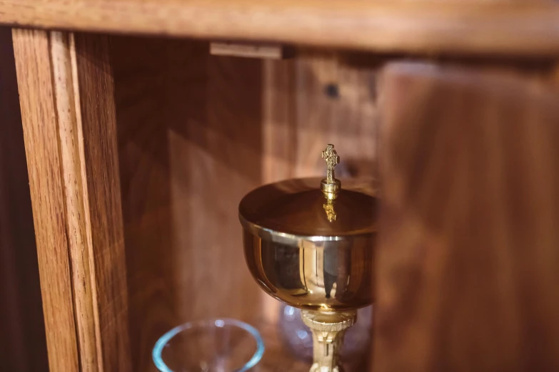 a golden cup sitting on top of a wooden shelf, unsplash, iconostasis in the bar, wooden cabinet, detailed zoom photo, overturned chalice