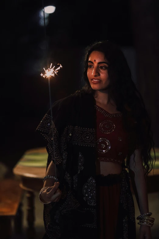 a woman holding a sparkler in her hand, wearing an elegant tribal outfit, film still dnd movie, ☁🌪🌙👩🏾, handsome girl