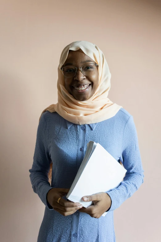 a woman in a blue dress holding a book, inspired by Maryam Hashemi, shutterstock contest winner, hurufiyya, wearing a pastel pink hoodie, jemal shabazz, student, very slightly smiling