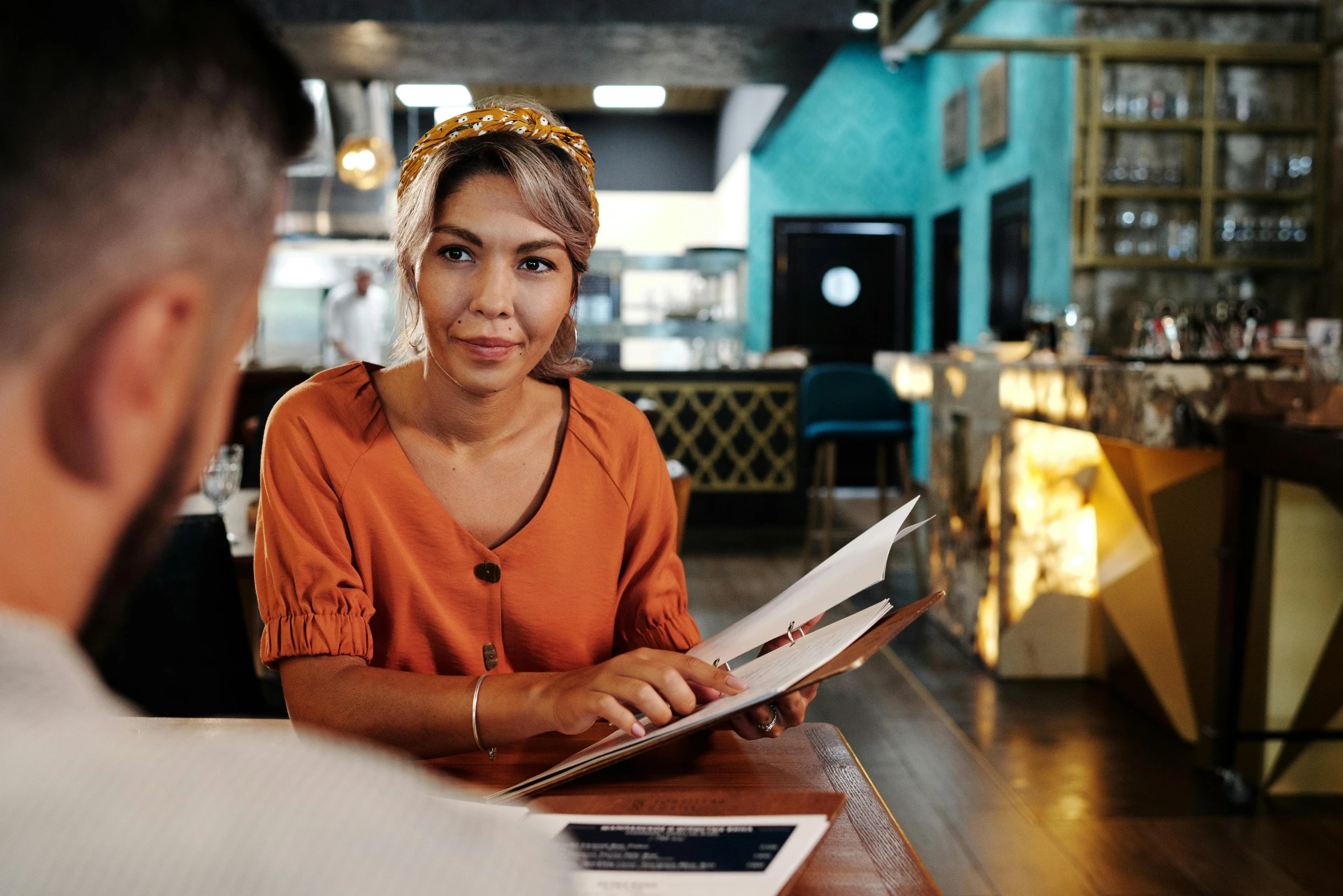 a man and woman sitting at a table in a restaurant, giving an interview, graphic print, looking straight ahead, an asian woman