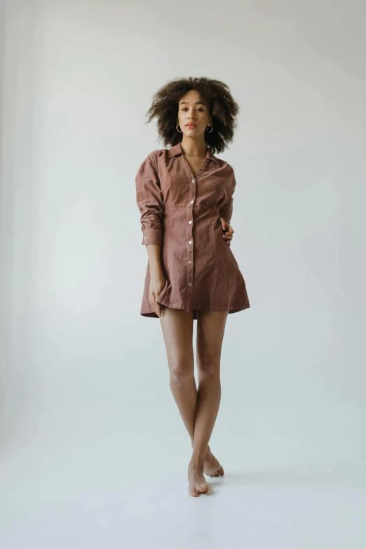 a woman standing in front of a white wall, unsplash, renaissance, wearing pajamas, short minidress, brown skinned, beth harmon