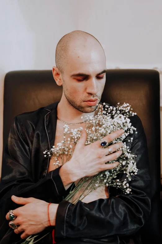 a man sitting in a chair holding a bunch of flowers, an album cover, inspired by Elsa Bleda, trending on unsplash, aestheticism, shaved head, wearing studded leather, embracing, young greek man