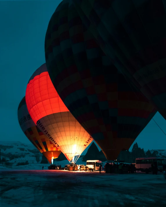 a couple of hot air balloons sitting on top of a field, out in the dark, snow glow, red and yellow light, on the runway