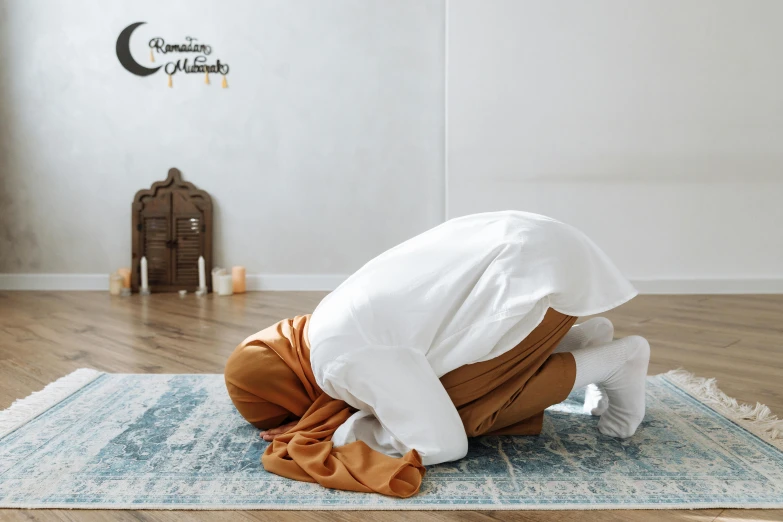 a person kneeling on a rug in a room, inspired by Sheikh Hamdullah, hurufiyya, asleep, caramel, white cloth, malaysian