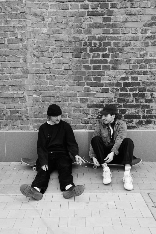 two men sitting on a bench next to a brick wall, a black and white photo, by Lee Gatch, unsplash, realism, plays skateboards, declan mckenna, in a square, cute boys