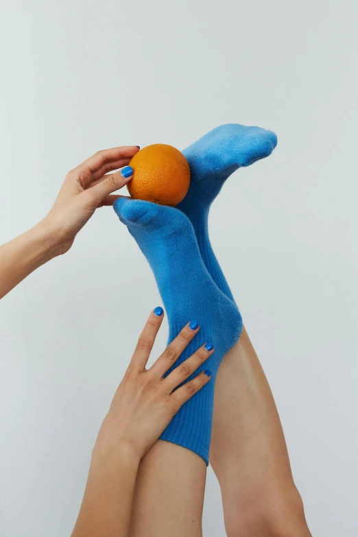 a person in blue socks holding an orange, inspired by Yves Klein, magic realism, silicone skin, soothing, coloured, fruit