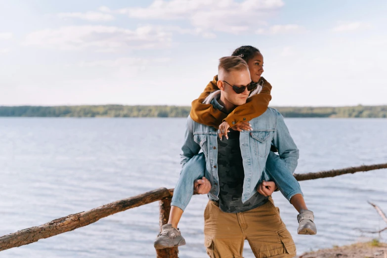 a man carrying a little girl on his shoulders, trending on pexels, an aviator jacket and jorts, on a lake, gay, non-binary