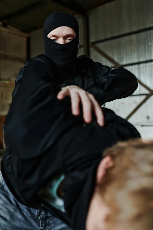 a man in a black hoodie is holding another man in a black hoodie, hurufiyya, getting ready to fight, jamie hewlet, medium-shot, burka