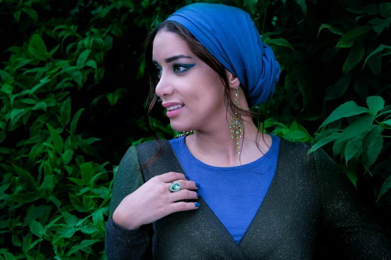 a woman standing in front of a bush wearing a blue turban, inspired by Yehia Dessouki, pexels contest winner, hurufiyya, earbuds jewelry, (night), jade green, various posed