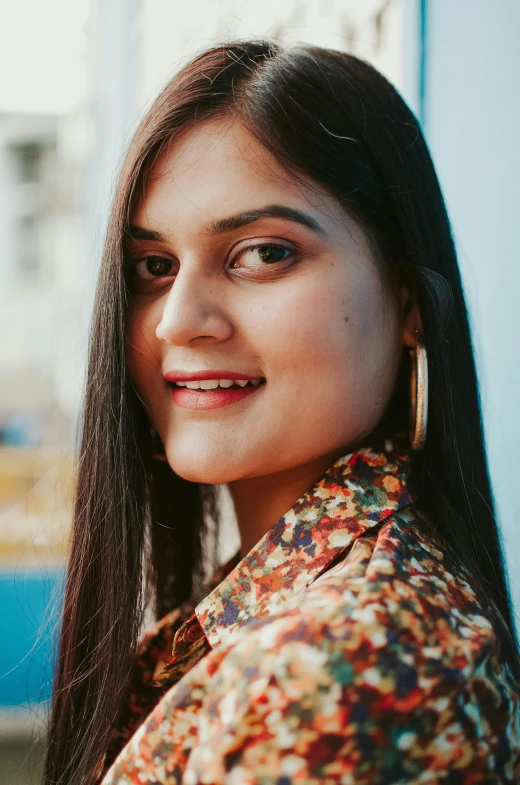 a woman standing in front of a blue wall, an album cover, pexels contest winner, indian girl with brown skin, headshot profile picture, portrait of happy a young woman, high angle closeup portrait