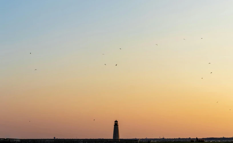 a lighthouse sitting on top of a beach next to a body of water, by Eglon van der Neer, pexels contest winner, minimalism, birds flying in the sunlight, sunset panorama, from wheaton illinois, seen from afar