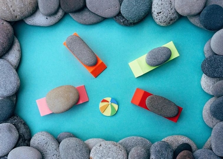 a group of rocks sitting on top of a blue surface, an album cover, inspired by Isamu Noguchi, unsplash, hoverboards, rainbow coloured rockets, laying on a beach, mini amphitheatre