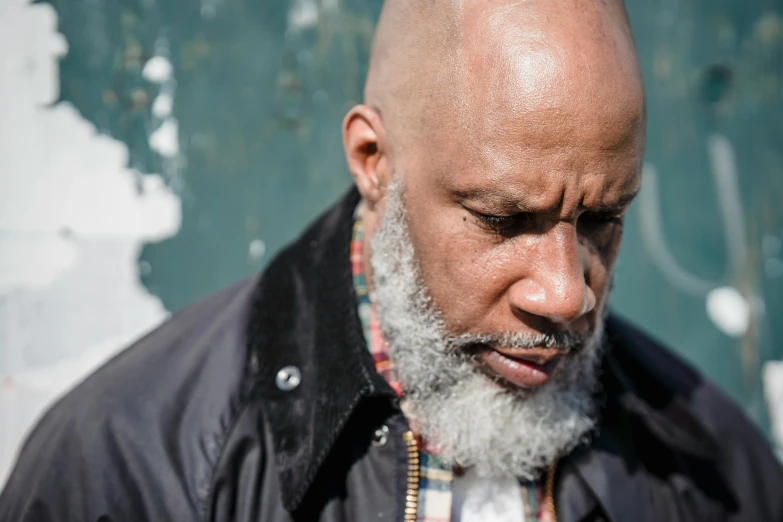 a bald man with a beard wearing a jacket, inspired by Mustafa Rakim, unsplash, gray hair and beard, musician, looking around a corner, atiba jefferson