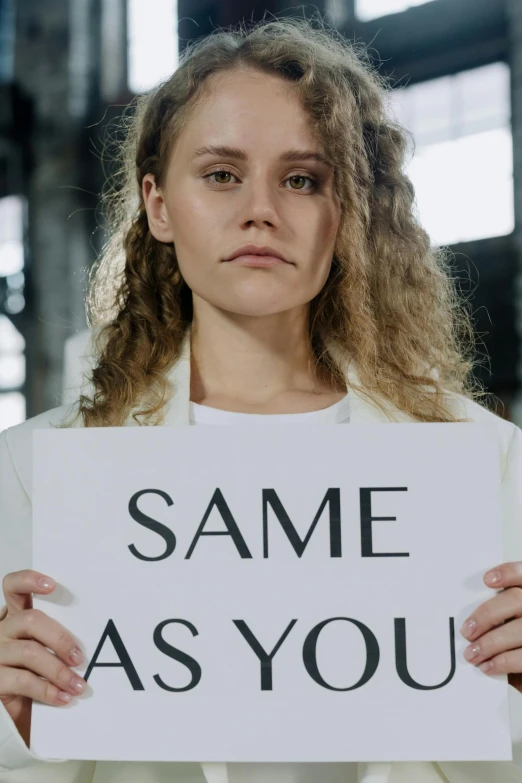 a woman holding a sign that says same as you, inspired by Vanessa Beecroft, unsplash, annasophia robb as joan of arc, yohji yamamoto, eleven/millie bobbie brown, profile image