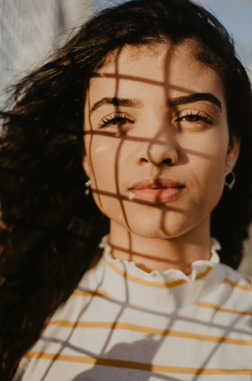 a close up of a woman's face behind a fence, a picture, by irakli nadar, trending on pexels, directional sunlight skewed shot, mixed race woman, square face, soft shadow