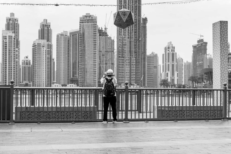 a black and white photo of a person standing on a bridge, inspired by Ruth Orkin, fine art, cairo, looking at his phone, in a cybercity, an arab standing watching over