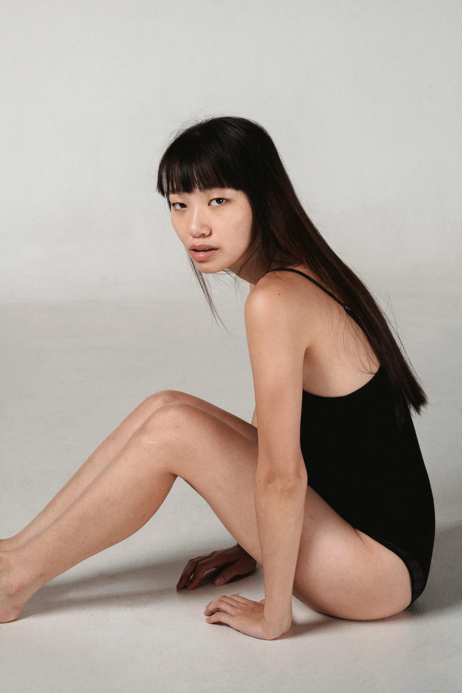 a woman sitting on the ground with her legs crossed, inspired by Fei Danxu, is wearing a swimsuit, long black hair in a ponytail, non binary model, side portrait imagery