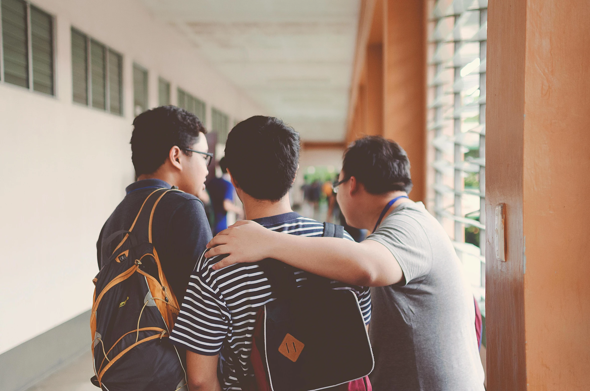 a group of young men standing next to each other, a picture, unsplash, happening, hunched shoulders, schools, two men hugging, looking her shoulder