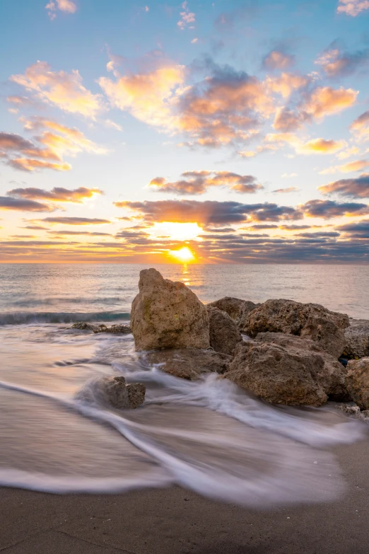 a large rock sitting on top of a sandy beach, by Robbie Trevino, sunrise, marbella, rock formations, miami beach