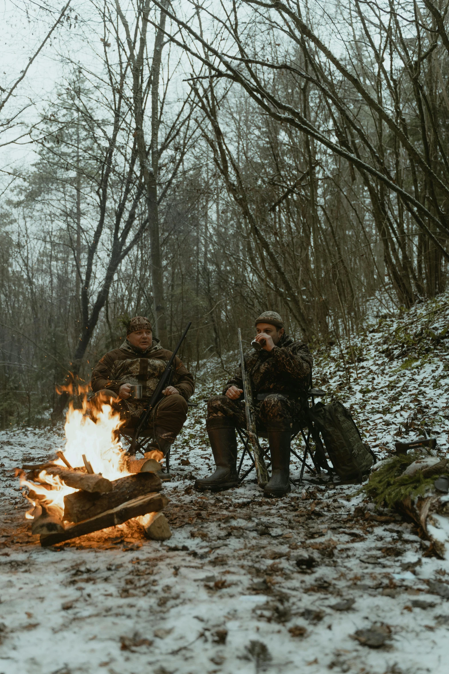 two men sitting around a campfire in the woods, by Adam Marczyński, hunters gear, in the winter, camo, cinestill