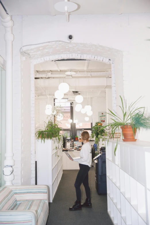 a person standing in a room with a suitcase, by Nina Hamnett, trending on unsplash, lush plants and lanterns, set inside of office, white sweeping arches, exiting store