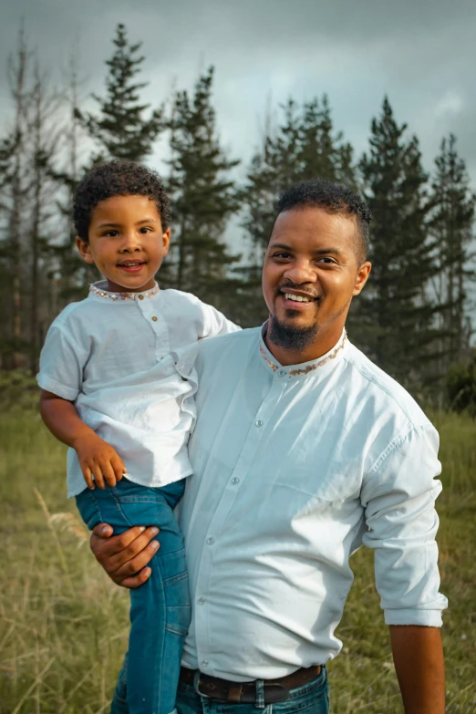 a man holding a small child in a field, an album cover, inspired by Ismail Gulgee, pexels contest winner, wearing a white button up shirt, avatar image, african canadian, headshot profile picture